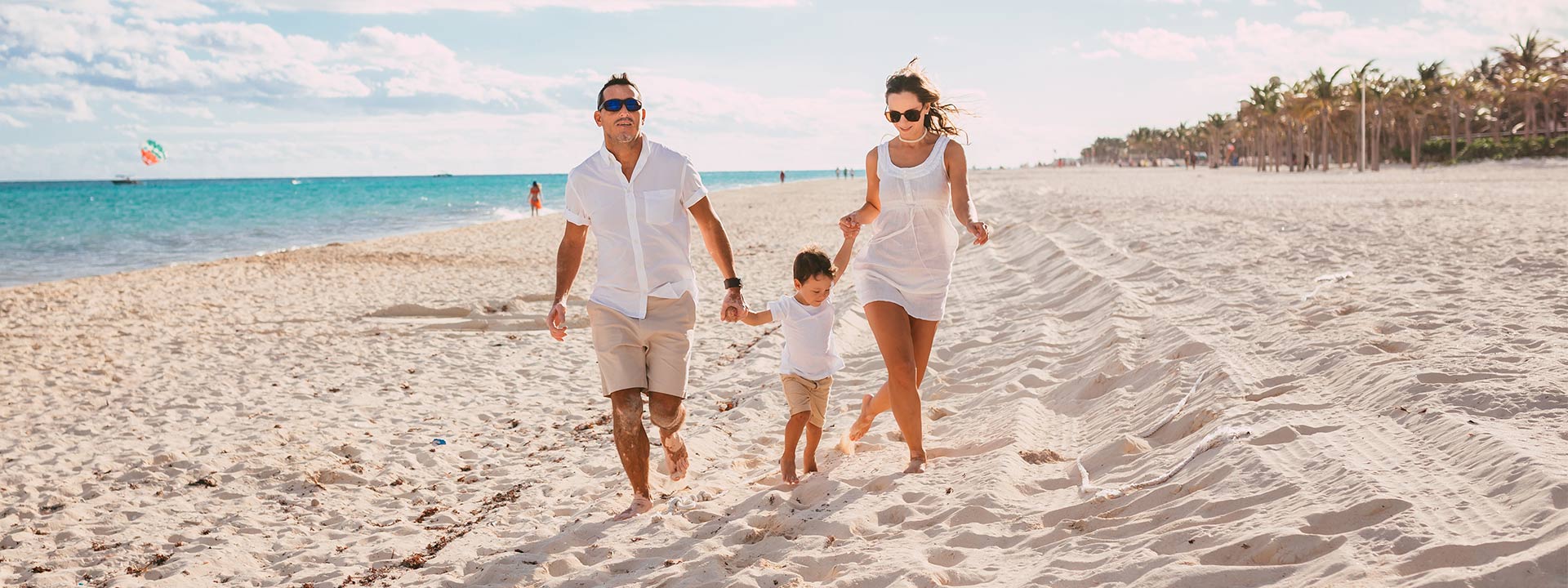 Pareja con su hijo caminando por la playa, disfrutando de un día soleado.