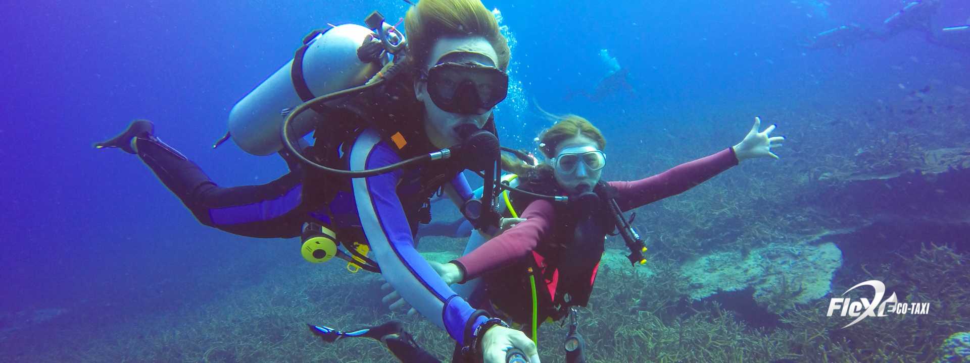 Couple scuba diving among colorful fish in crystal-clear water, smiling and enjoying the underwater experience.