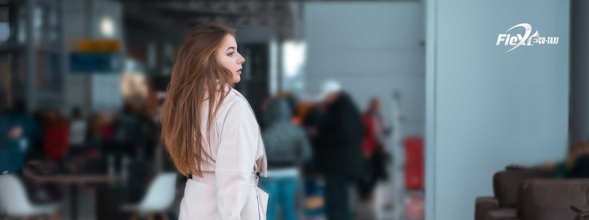Woman with a carry-on suitcase waiting for her flight at the airport, looking at the departures board.